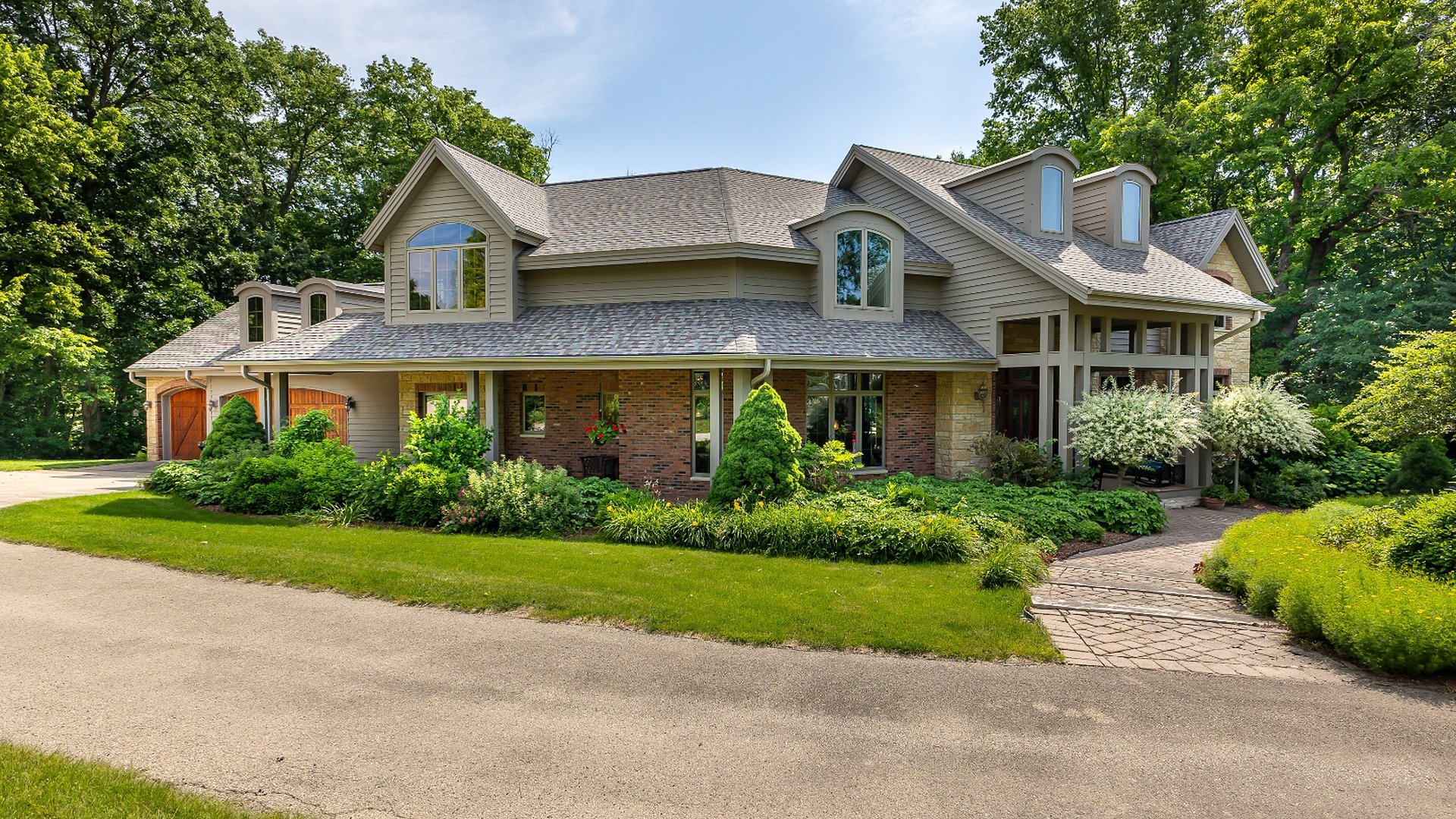 82 Ford Drive East Dubuque — luxury home exterior with stone and wood garage doors, lush landscaping